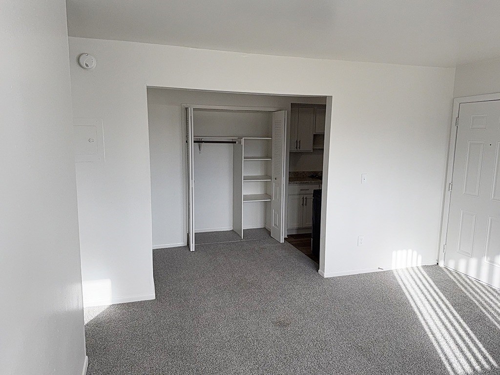 A living and dining room with a closet with shelves and carpet at Waverly Park Apartments, Lansing