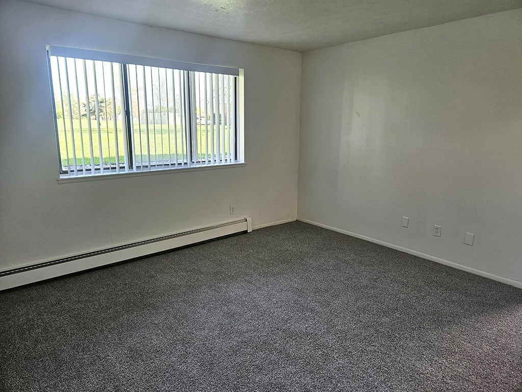 A living room with a carpeted floor and a window with blinds at Waverly Park Apartments, Lansing