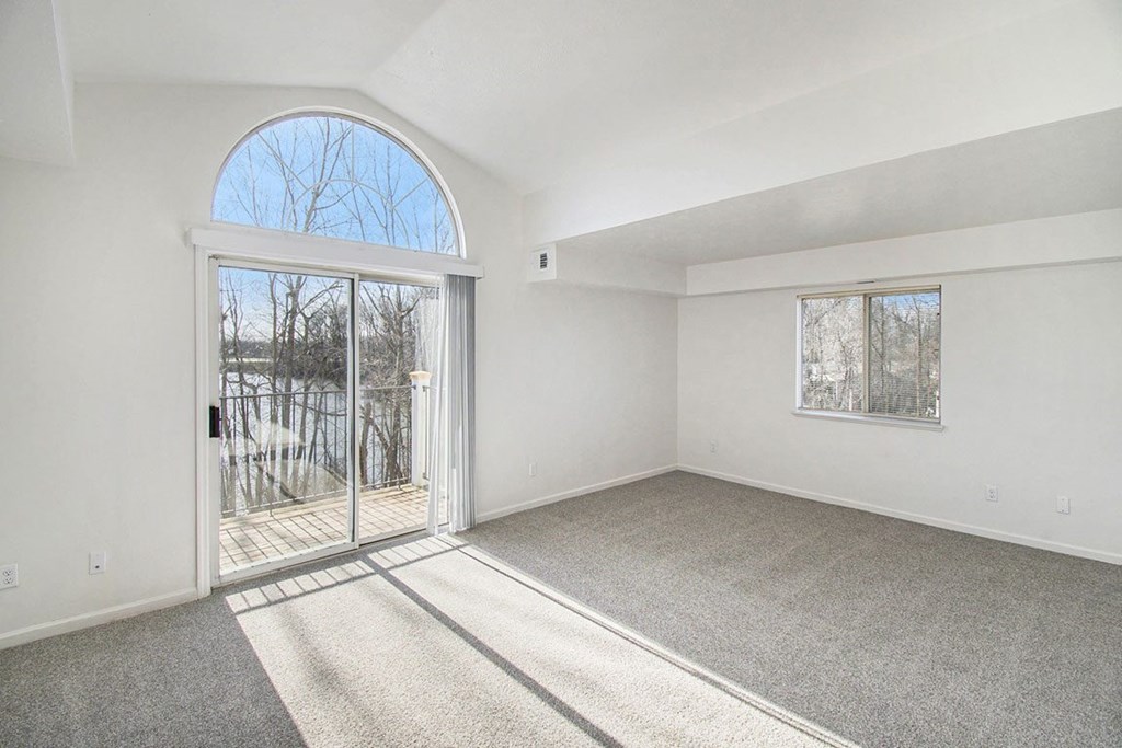 A living room with a cathedral ceiling, large arched window and a slider to a balcony at West Hampton Park Apartments in Elkhorn, NE 68022