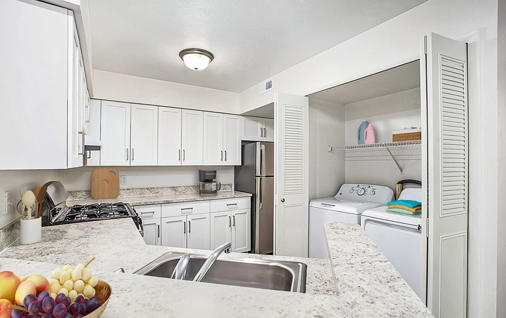 A kitchen with a breakfast bar, white cabinets and a washer/dryer at West Hampton Park Apartments in Elkhorn, NE 68022