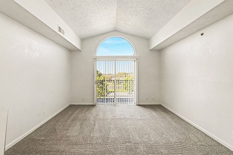 A living room with a cathedral ceiling, sliding glass doors and a grey carpet at West Hampton Park Apartments in Elkhorn, NE 68022