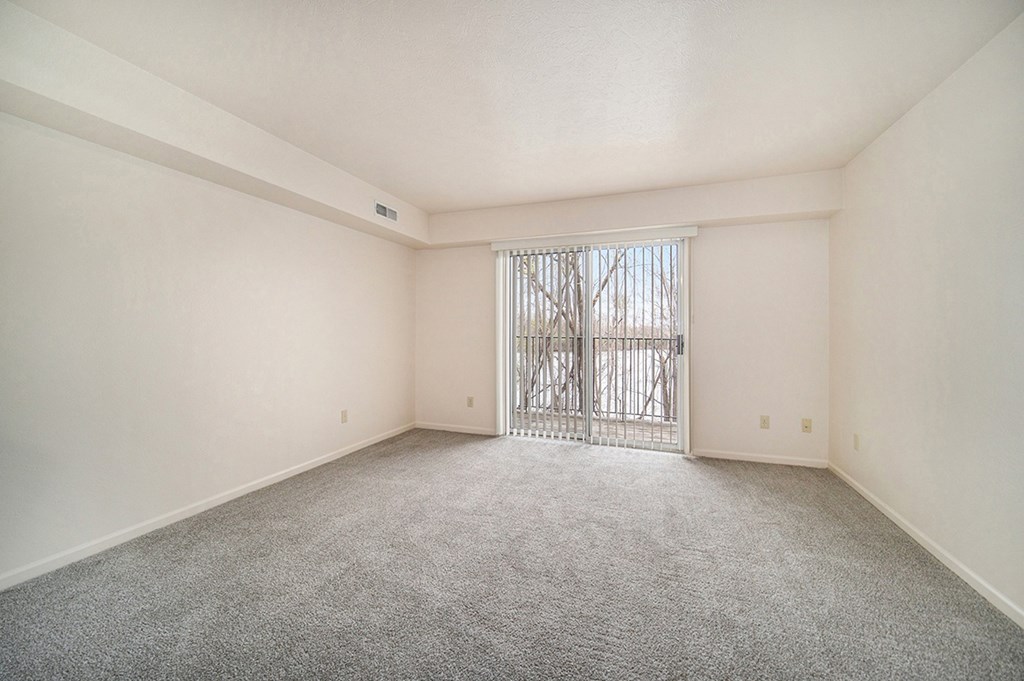 A living room with a carpeted floor and a slider to a balcony at West Hampton Park Apartments in Elkhorn, NE 68022