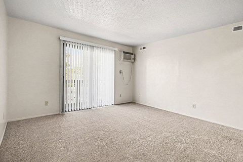 A room with a carpeted floor and a window with blinds.