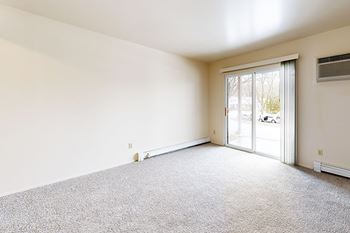 A living room with a carpeted floor and a slider to a private patio at Wood Creek Apartments, Kenosha, WI, 53144