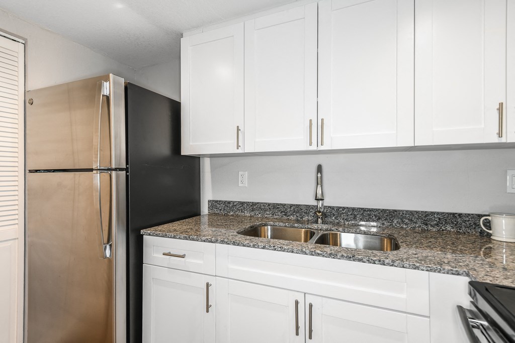 a kitchen with white cabinets and granite counter tops and a stainless steel refrigerator