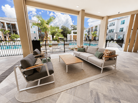 A patio with a couch, chair, and table with a pool and buildings in the background.