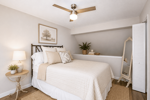 A bedroom with a bed, a ceiling fan, and a nightstand with a lamp.