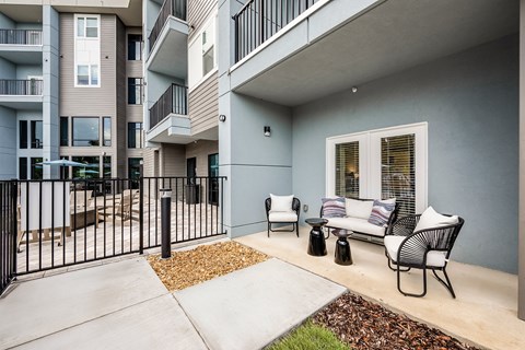 A patio with a couch, chairs, and a table is in front of a building.