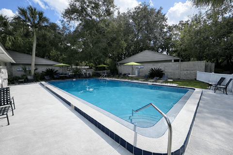 A swimming pool surrounded by trees and a white fence.