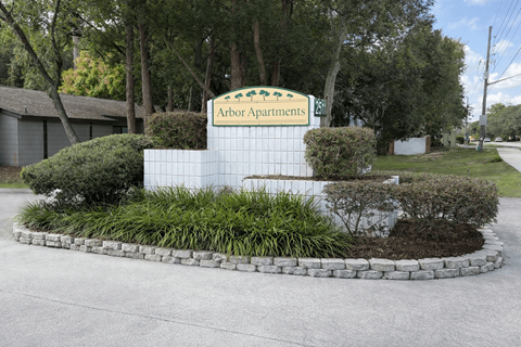 A sign for Arbor Apartments is surrounded by bushes and trees.