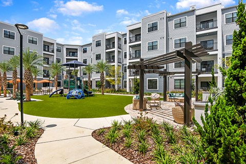 A sunny day at a modern apartment complex with a playground and landscaped courtyard.