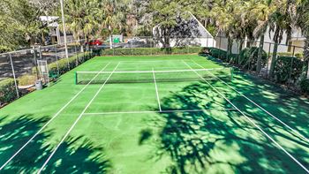 A tennis court surrounded by trees and a fence.