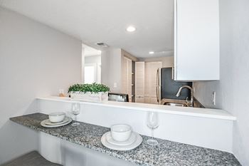 A kitchen counter with a plant, a bowl, and a glass of wine on it.