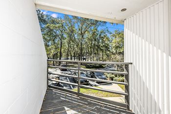 A white building with a balcony overlooking a parking lot and trees.