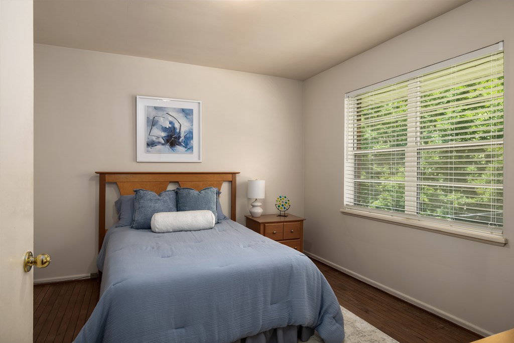 A bedroom with a bed, nightstand, and a window with blinds.