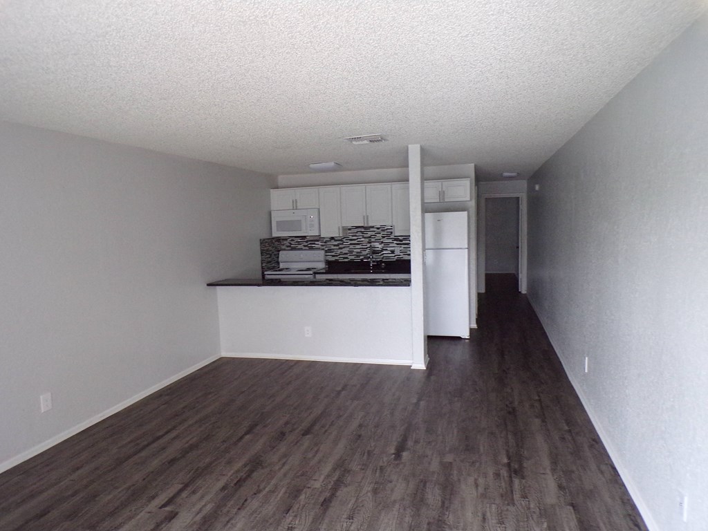 an empty living room and kitchen with a wood floor
