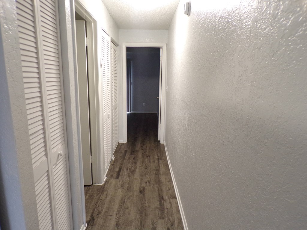 a hallway with white shutters and a door to a dark room