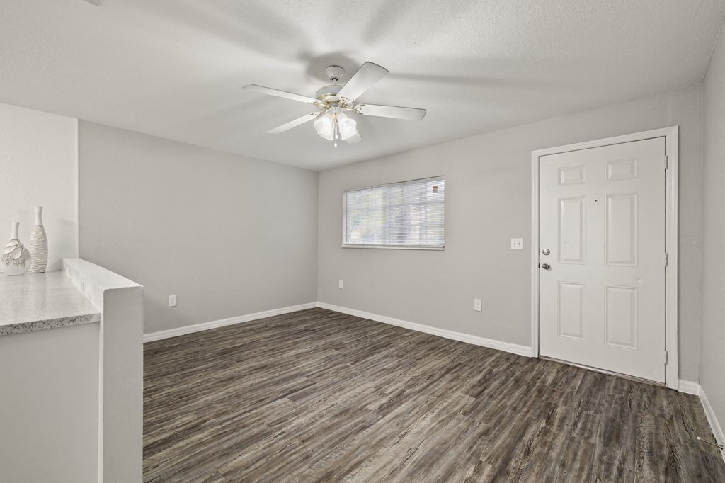 an empty living room with a white door and a ceiling fan