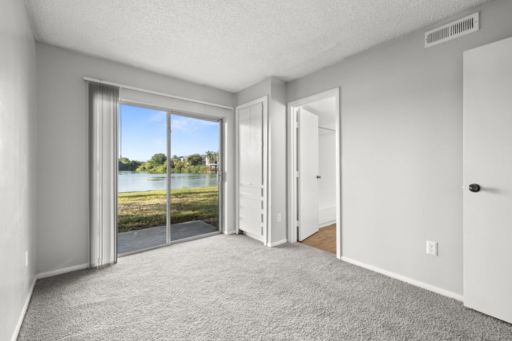 A room with a carpeted floor and a sliding glass door leading to a view of a lake.