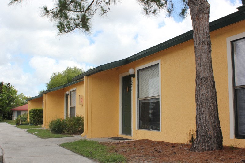 a yellow building with a sidewalk and a tree in front of it