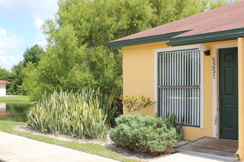 a small yellow house with a sidewalk and plants in front of it