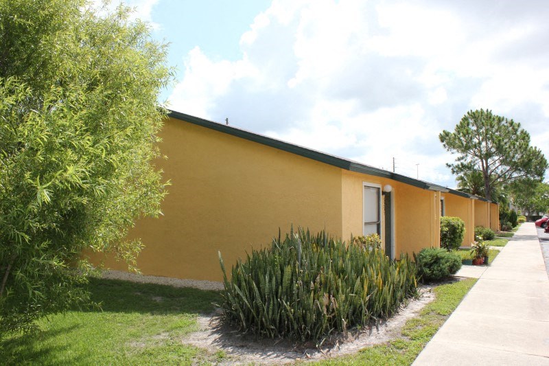 a yellow building with a sidewalk and plants in front of it