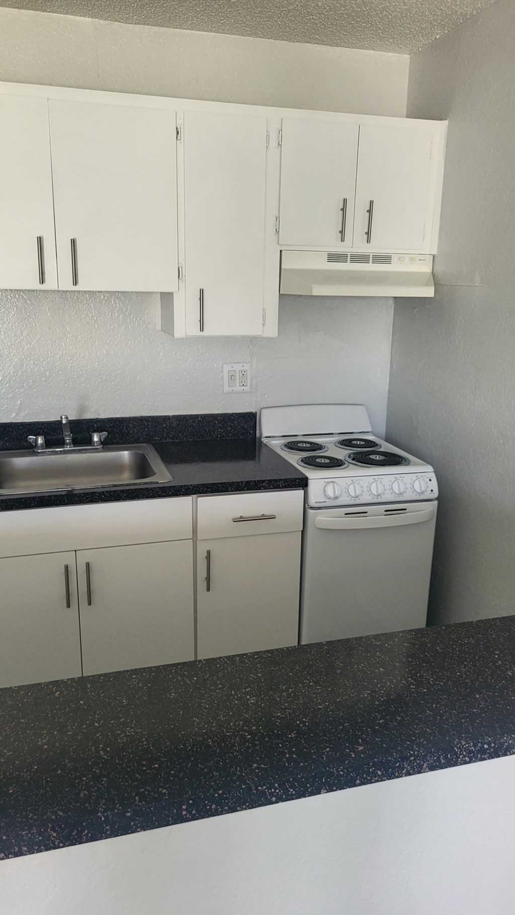 A kitchen with white cabinets and a black countertop.