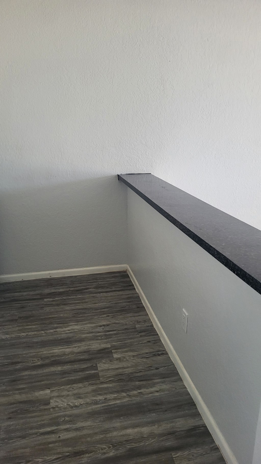 A corner of a room with a wooden floor and a black trim.