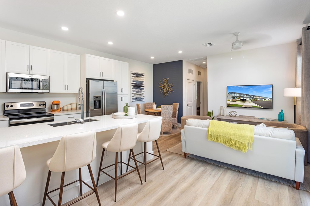 A modern kitchen with white countertops and a white sofa with a yellow throw.