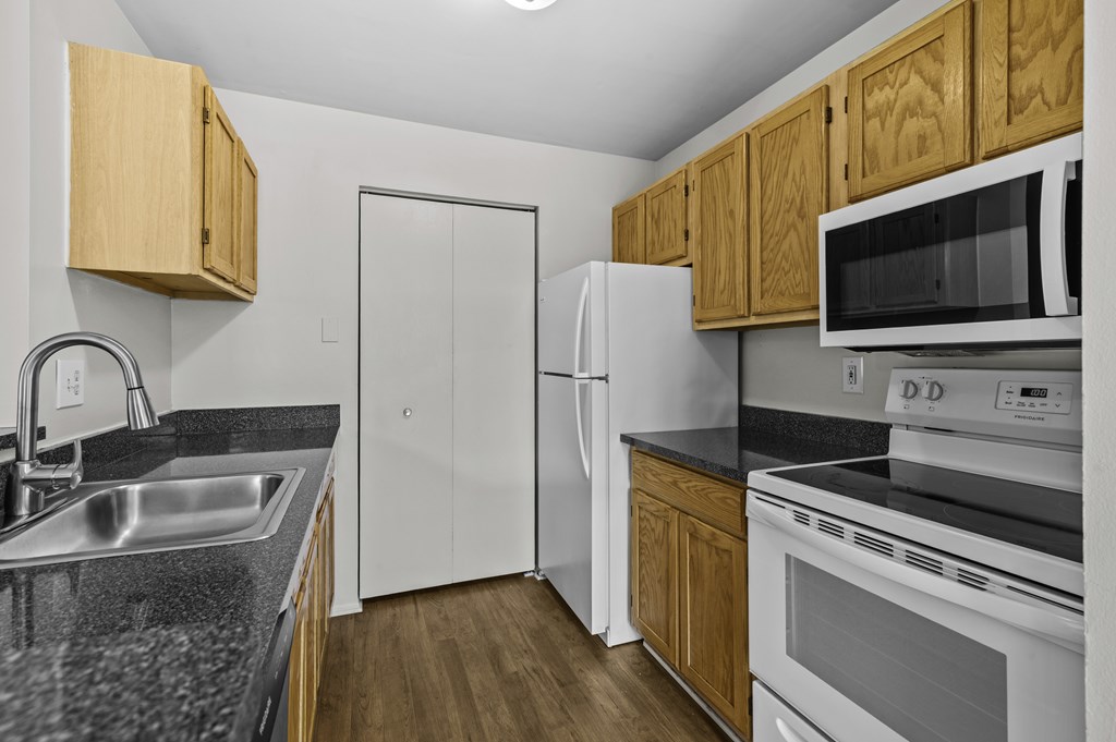 A kitchen with a white refrigerator, black countertops, and wooden cabinets.