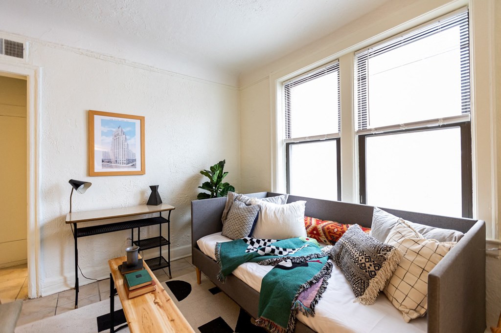a living room with a couch and a bed and three windows