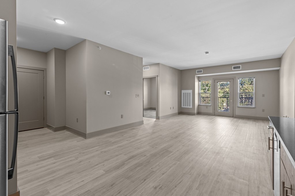 A spacious room with wooden flooring and a large window with a view of trees.