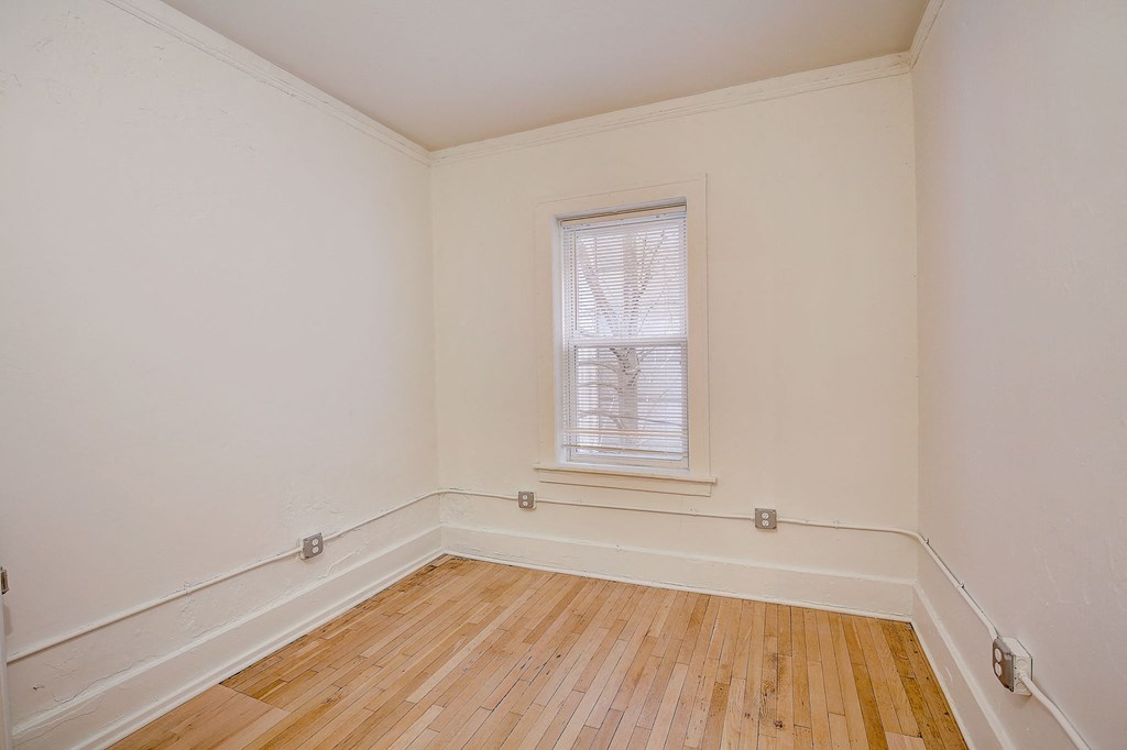 a bedroom with hard wood floors and window and white walls