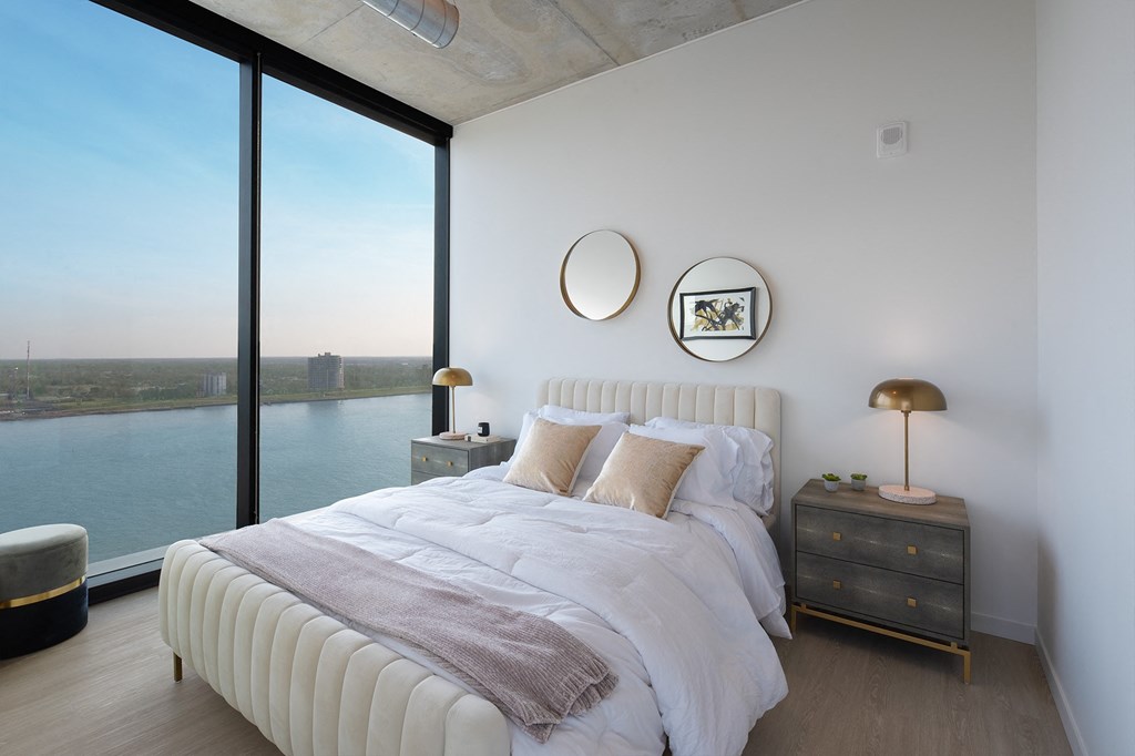 a bedroom with a large window and a bed with white sheets and pillows