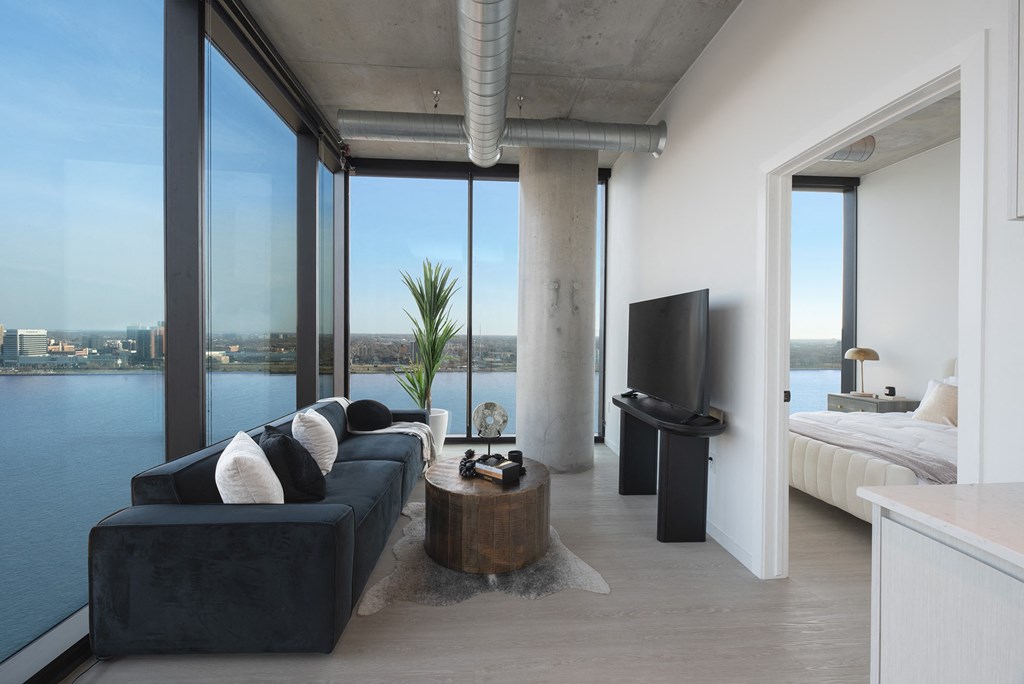 a living room with a black couch and a television and a view of the water