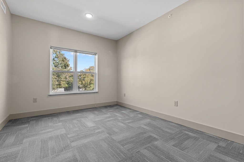 A room with a large window and a grey carpet.