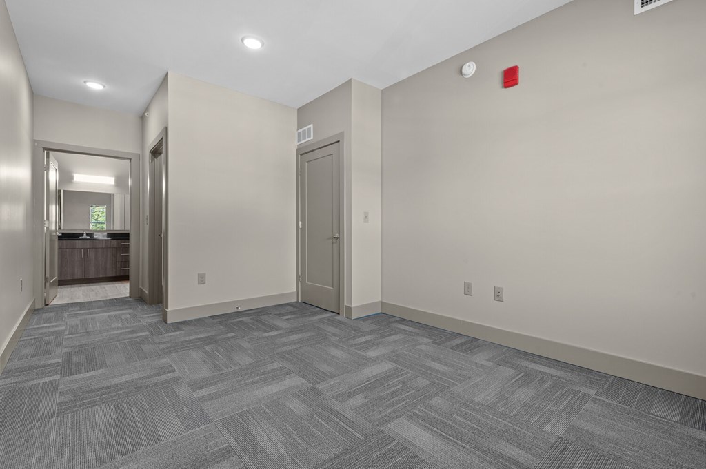 A hallway with a grey carpet and a red fire alarm on the wall.