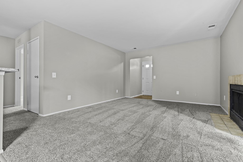 A large, empty room with a fireplace and carpeted floor.