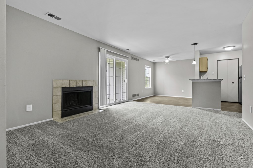 A spacious living room with a fireplace and a grey carpet.