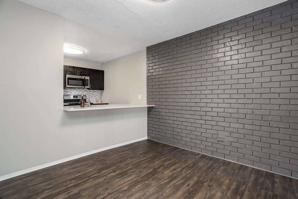 an empty living room with a brick wall and a kitchen