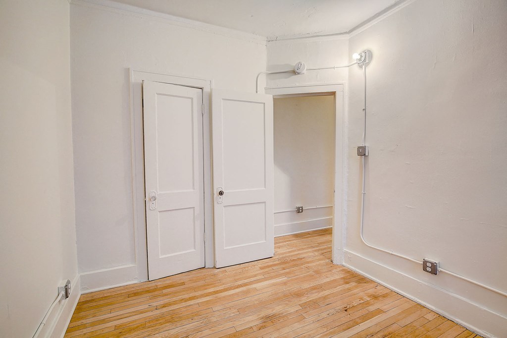 a bedroom with white walls and wood floors and two doors