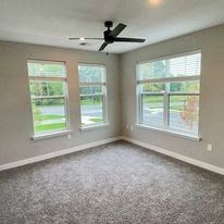 an empty bedroom with a ceiling fan and three windows