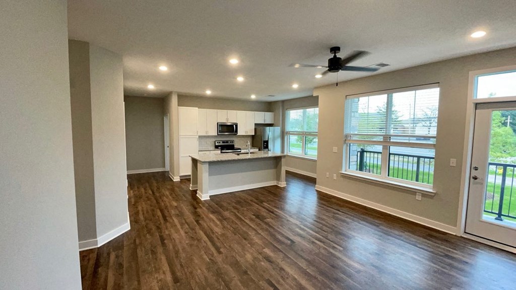 an empty living room with a kitchen and a ceiling fan