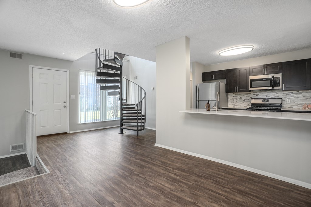 an empty living room with a kitchen and a spiral staircase
