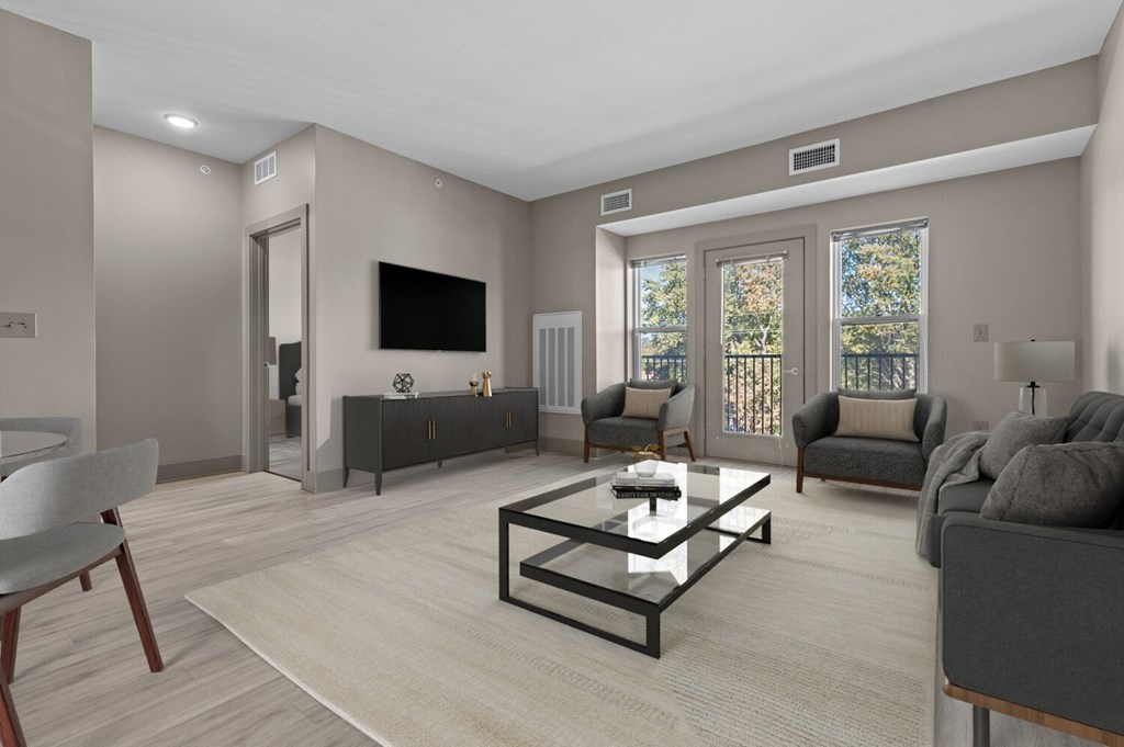 A modern living room with a grey sofa, a glass coffee table, and a flat-screen TV mounted on the wall.