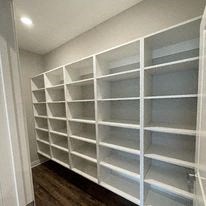 a walk in closet with white shelves and