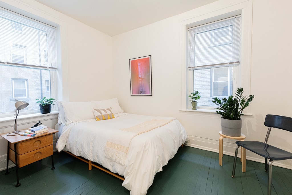 a bedroom with a bed and a chair and two windows