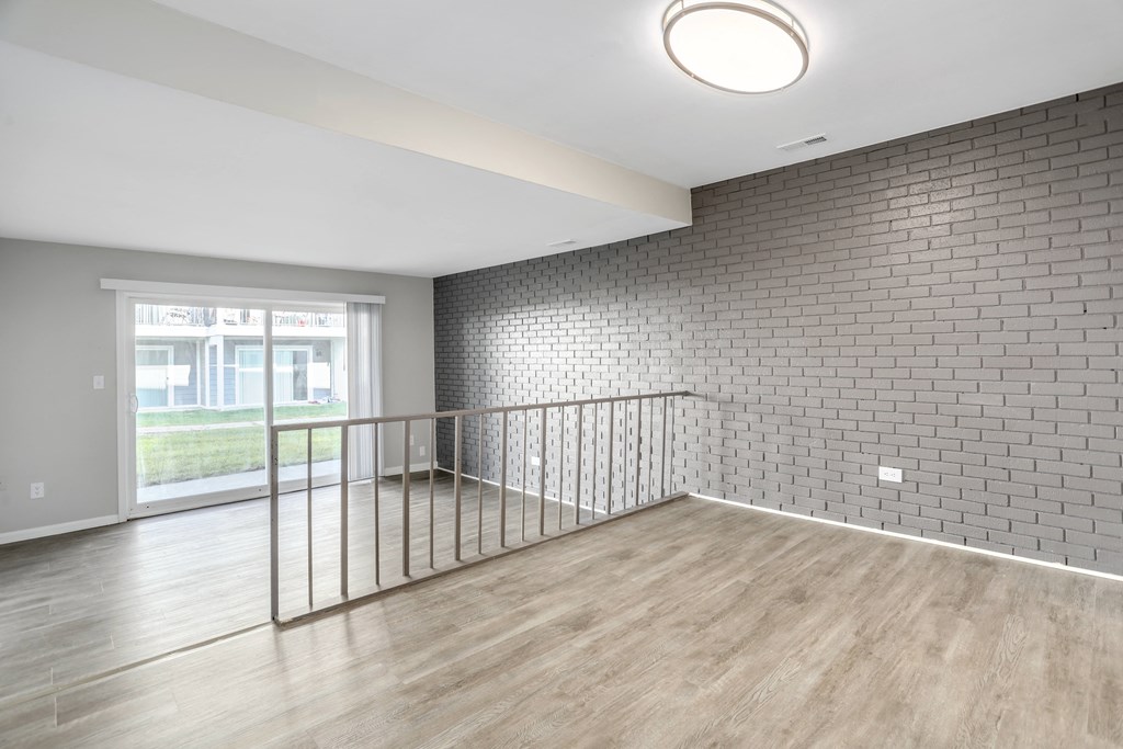 an empty living room with a brick wall and wood floors