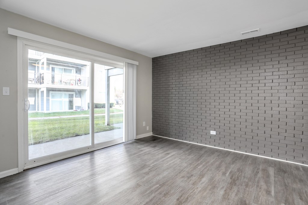 an empty living room with wood floors and a brick wall