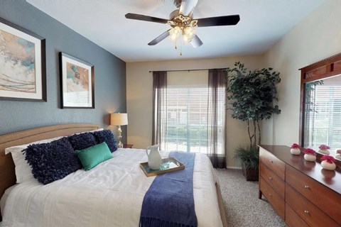 A bedroom with a bed, a ceiling fan, and a nightstand with flowers.